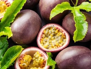 Whole and halved passion fruits with yellow pulp, nestled among green leaves and Jasmine 'Angel Wings' blooms in an 8" pot.