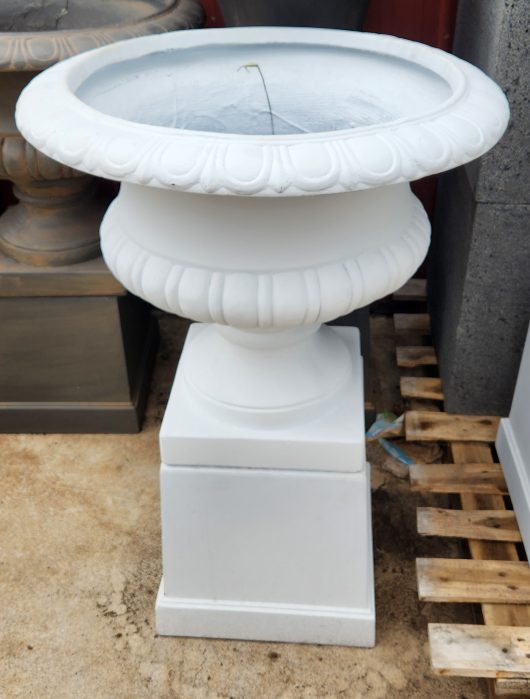 A GardenLite Wide Urn White 63x56cm sitting on a pallet in a yard.