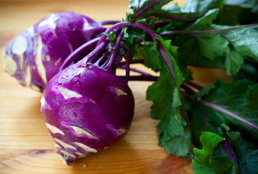 Two vibrant purple kohlrabi bulbs with green leaves attached, artfully arranged on a wooden surface, showcase the beauty of Kohlrabi 4" Pot (Copy).