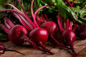 Freshly harvested Beetroot 'Bull's Blood' 4" Pot boasts vibrant leafy green tops, resting on a wooden surface, ready to enhance your garden.