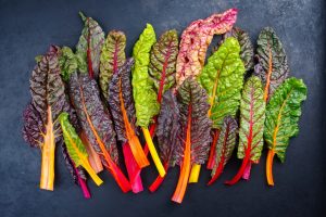 A variety of fresh, multicolored Swiss chard leaves arranged on a dark surface.