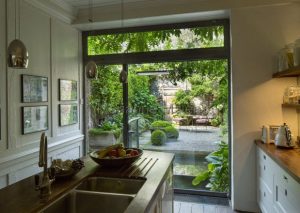 A kitchen with a sink island, countertop appliances, and a window door opening to a lush garden with seating and thoughtful garden design.