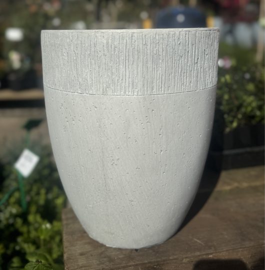 A GeoLite Tall planter in Egg White Wash, measuring 29x34cm, stands on a wooden surface with blurred greenery in the background.