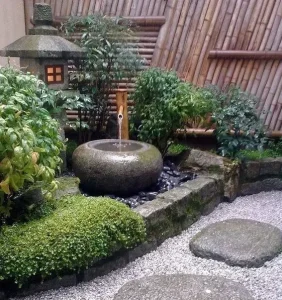 A serene Japanese garden with a stone water fountain, surrounded by green foliage, bamboo fencing, and a thoughtfully crafted stone pathway—a perfect example of exquisite garden design.