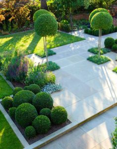 A garden with expertly crafted garden design features, including neatly trimmed bushes, spherical topiaries, and geometric paving stones leading through lush greenery.