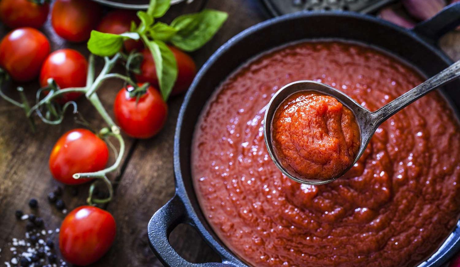 A ladle scoops tomato sauce from a cast iron skillet, with fresh tomatoes and basil on the side. It's a comforting moment that makes you momentarily forget about garden design problems.