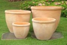 The Terracotta Rim Egg Traditional 23x19cm plant pots, arranged in varying sizes with a ribbed design, are displayed on a grassy lawn with greenery in the background.