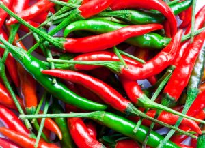 A close-up of a pile of red and green chili peppers with stems, arranged in a scattered pattern.