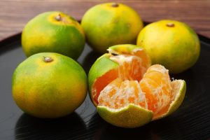 Five vibrant citrus 'Hickson' mandarins, one peeled and four whole, rest elegantly on a dark surface.