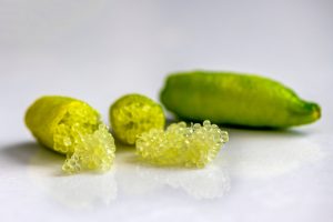 Close-up of finger limes with one cut open, revealing pearl-like citrus vesicles on a smooth white surface.