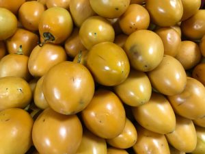 A vibrant pile of ripe Solanum 'Tamarillo' Red (Copy) catches the eye, stacked closely together with a hint of orange-yellow peeking through.