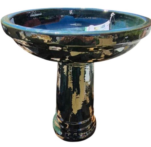 The Sorrento Birdbath features a tall glazed ceramic design with a deep blue basin and column pedestal, adorned in an iridami pattern of mottled green and brown hues. Size: 46x60cm.