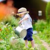 In a colorful garden, a child in a straw hat and blue shorts discovers the many benefits of gardening while watering plants with a silver can.